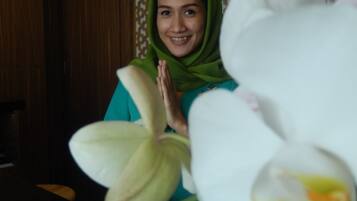 A person in a green headscarf sitting in front of a white orchid.