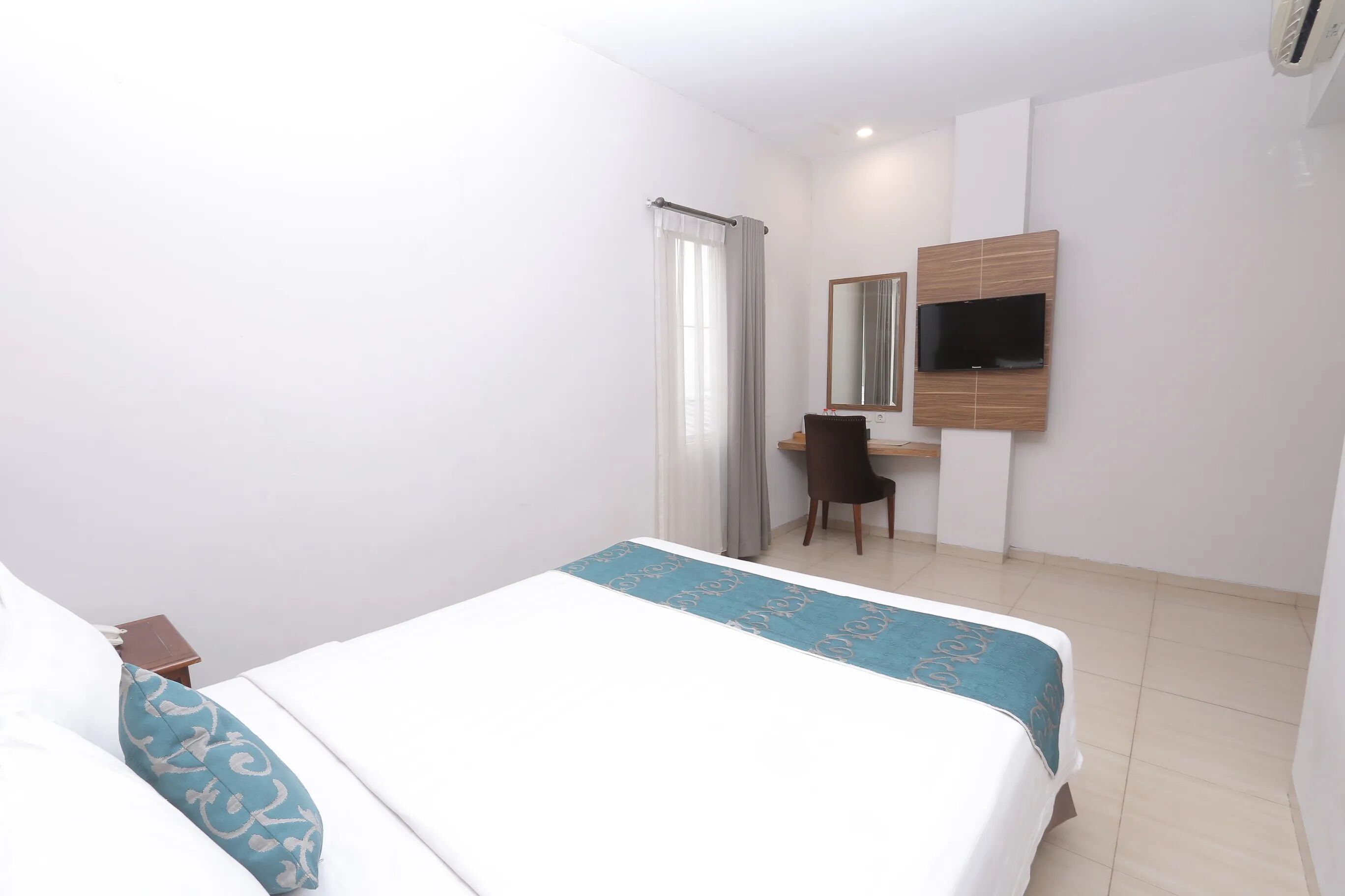 Een hotelkamer met een bed, een bureau, een stoel, een televisie en een raam met gordijnen.