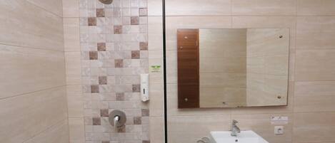 Une salle de bain équipée d’une douche, d’un lavabo, d’un miroir et d’un distributeur de savon.