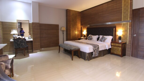 A spacious bedroom with a large bed, bedside tables, a desk, and a chair. - Grand Amira Hotel (Surakarta)