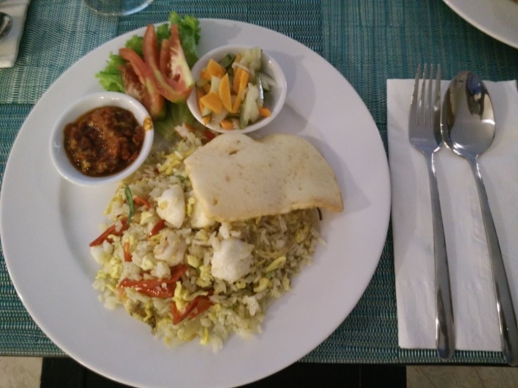 A plate of food with rice, vegetables, and a piece of flatbread, accompanied by a small bowl of sauce and a salad.