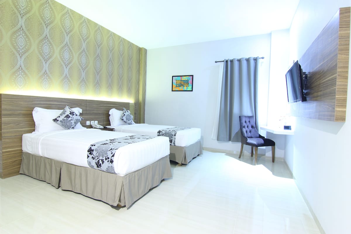 A hotel room with two beds, a TV, a chair, and a curtain.
