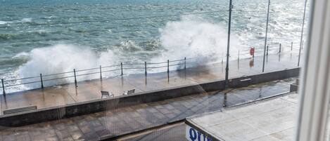Un paseo marítimo con barandilla, un cartel que dice "QUEENS HOSPITAL" y olas rompiendo en la orilla.