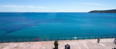 A coastal promenade with a clear view of the sea, a pedestrian path, and a cyclist.