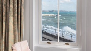 A room with a large window overlooking the sea, a chair, and a small table. - The Queens Hotel (Penzance)