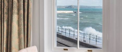 Una habitación con un amplio ventanal con vista al mar, una silla y una pequeña mesa.