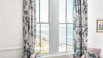 Una habitación de hotel con una cama, dos sillas, una mesita y vista al océano.