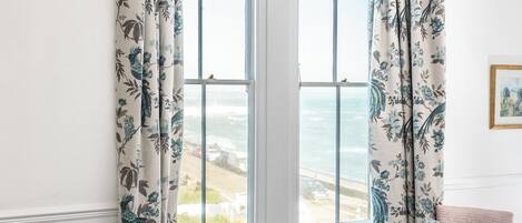 A hotel room with a bed, two chairs, a small table, and a view of the ocean.