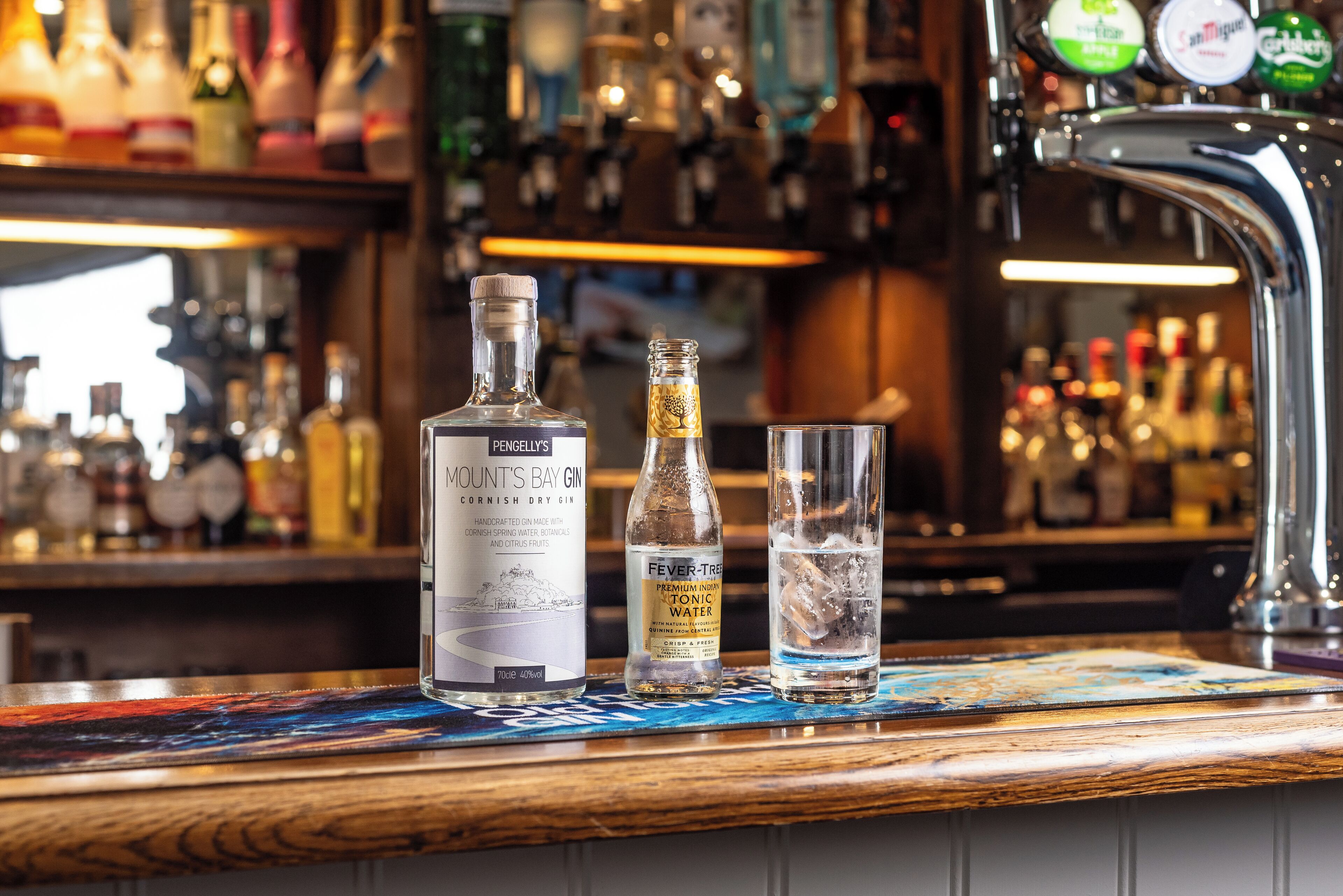 Una barra amb ampolles de ginebra Pengeley's Mount's Bay i Fever Tree Premium Iced Tonic, i un got d'aigua.