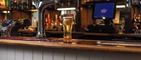Un bar con una grifo, una cerveza en un vaso y varias botellas al fondo.
