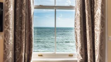 A window with curtains, a view of the sea, and a white sill.