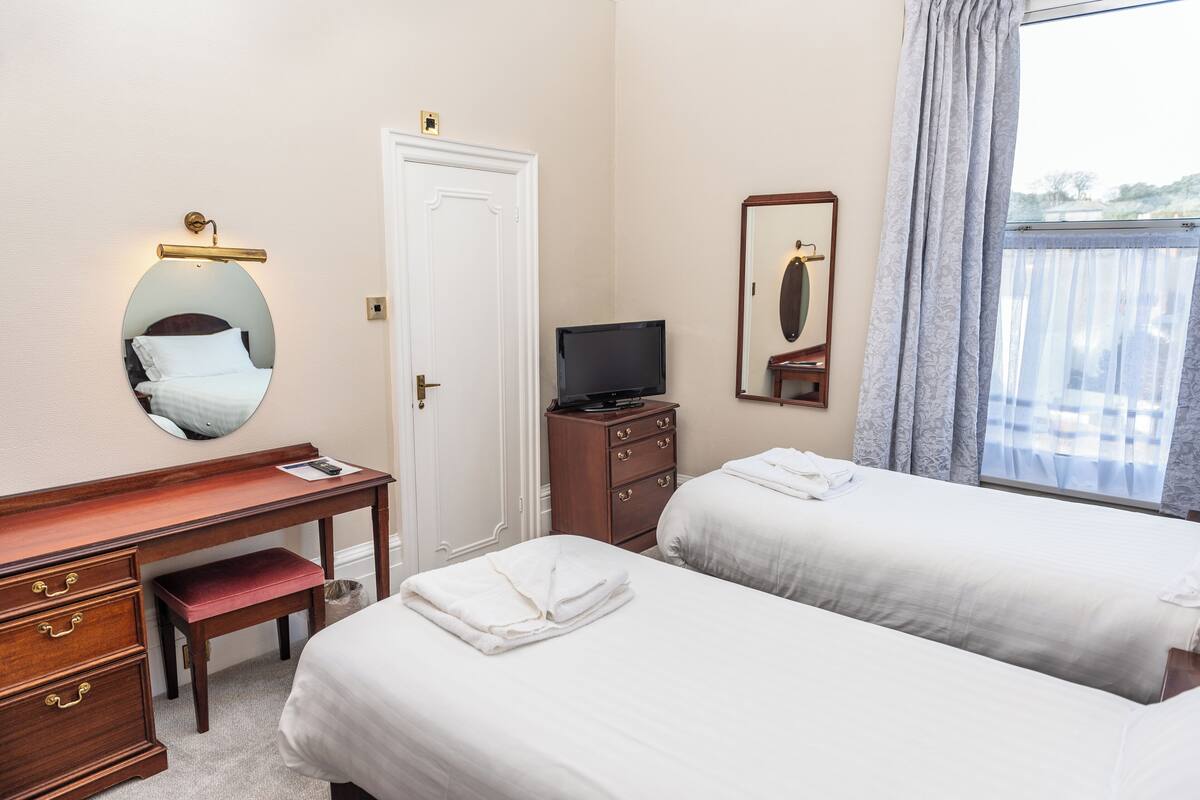 Habitación de hotel con dos camas, un escritorio con cajones, un televisor, un espejo y una ventana con cortinas.