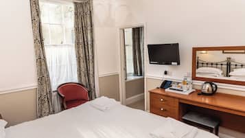 A hotel room with a bed, a desk with a television, a mirror, and a red chair.