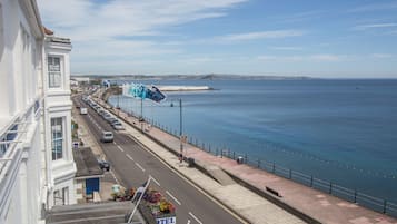 Una carretera costera con un hotel llamado "HOTEL" a la izquierda, un cielo azul despejado y el mar al fondo.
