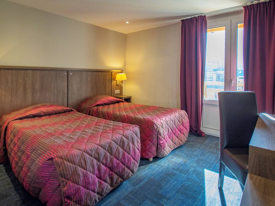 Ein Hotelzimmer mit zwei Betten, einem Schreibtisch, einem Stuhl und einem Fenster mit Vorhängen.