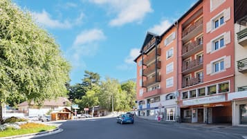 Une vue de rue avec une voiture bleue en mouvement, des immeubles dotés de balcons et un hôtel appelé « HÔTEL MONTR-BRISON ».