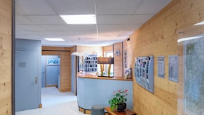 A reception area with a wooden wall, a reception desk, a seating area with a table and chairs, and a large map on the wall. - Hôtel Mont-Brison (Briançon)