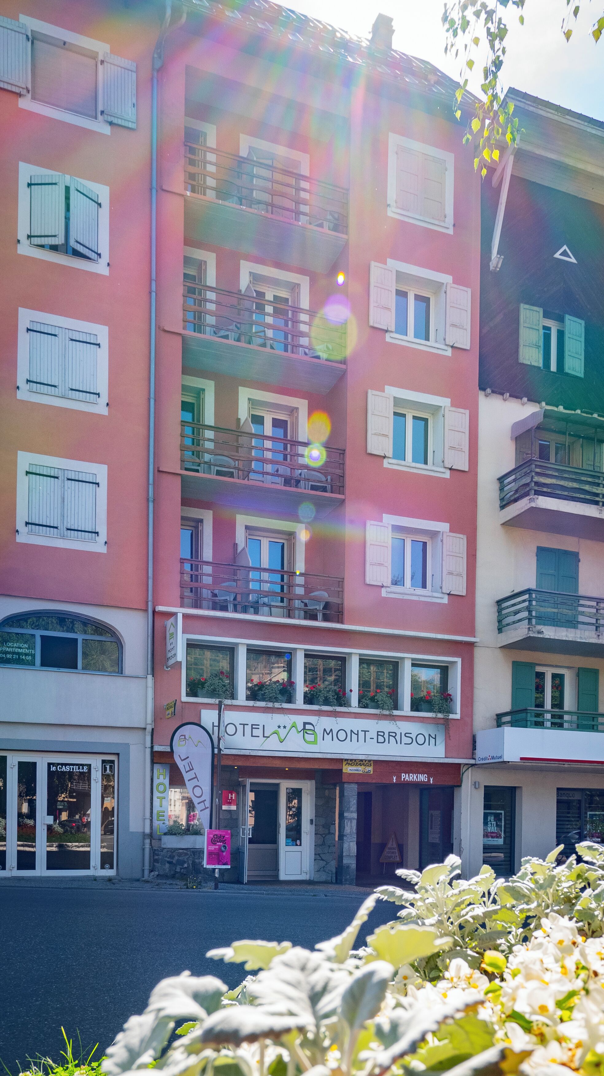 Un hotel de varios pisos con balcones, un cartel que dice "HOTEL MONT-BRISORY" y una señal de estacionamiento.