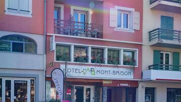 Un hotel de varios pisos con balcones, un cartel que dice "HOTEL MONT-BRISORY" y una señal de estacionamiento.