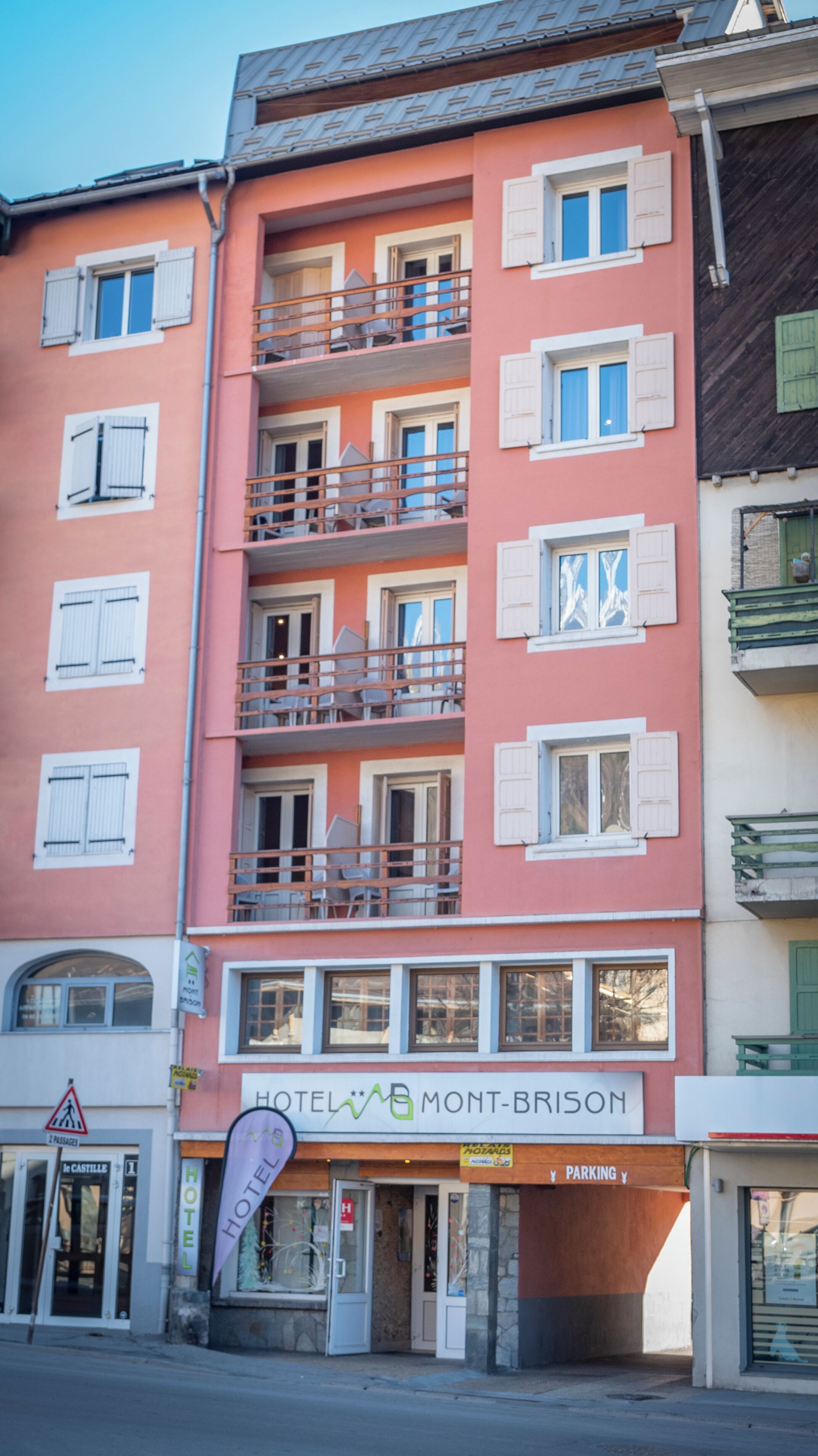 Un hotel a più piani con balconi, un cartello con su scritto "HOTEL MONT-BRISON" e un segnale di parcheggio sottostante.