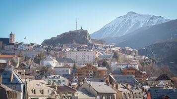 A town with historic buildings, a prominent hilltop structure, and a mountain backdrop.
