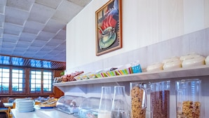 A buffet with various food items, including bowls of soup and a glass pitcher of water, arranged on a counter with a tiled floor and a window in the background. - Hôtel Mont-Brison (Briançon)