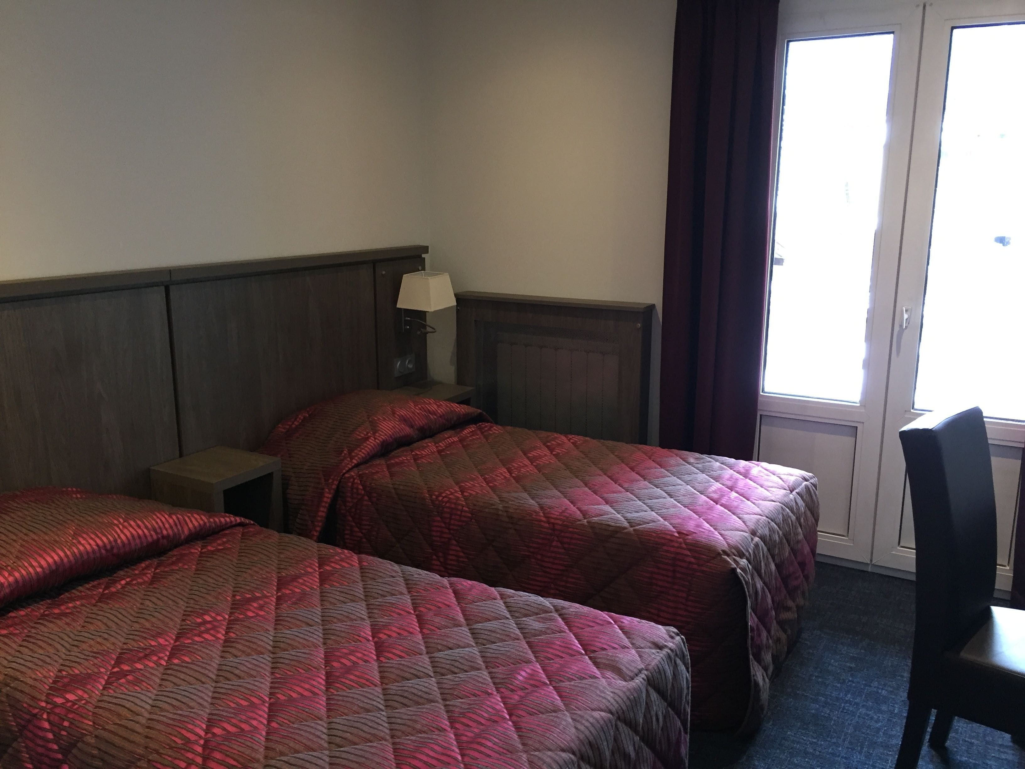 Una habitación de hotel con dos camas, una mesita de noche, una lámpara y una silla.