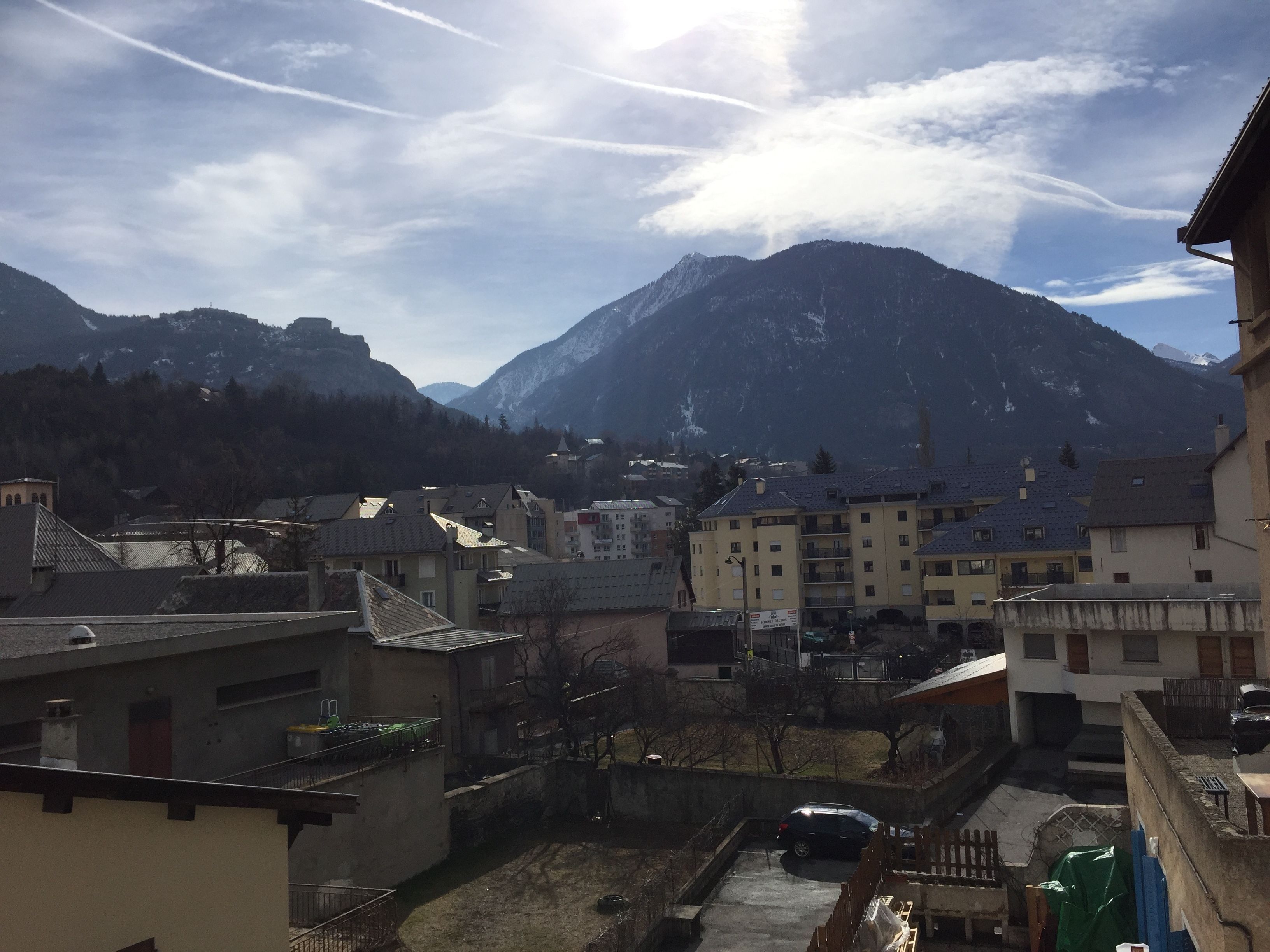 Un quartier résidentiel avec des immeubles, une voiture et des montagnes en arrière-plan.