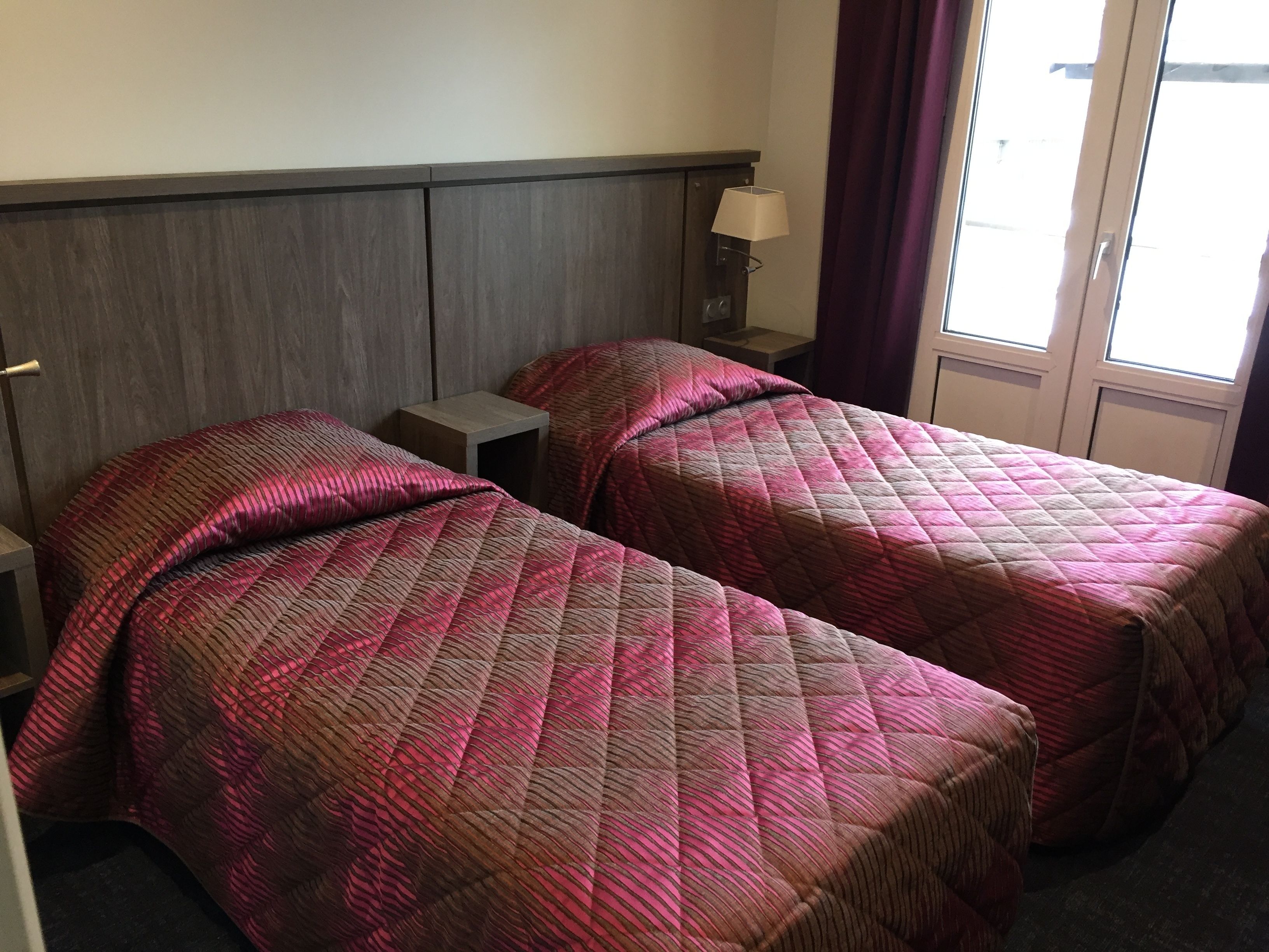 Una camera d'albergo con due letti, un comodino, una lampada e una finestra con tende.