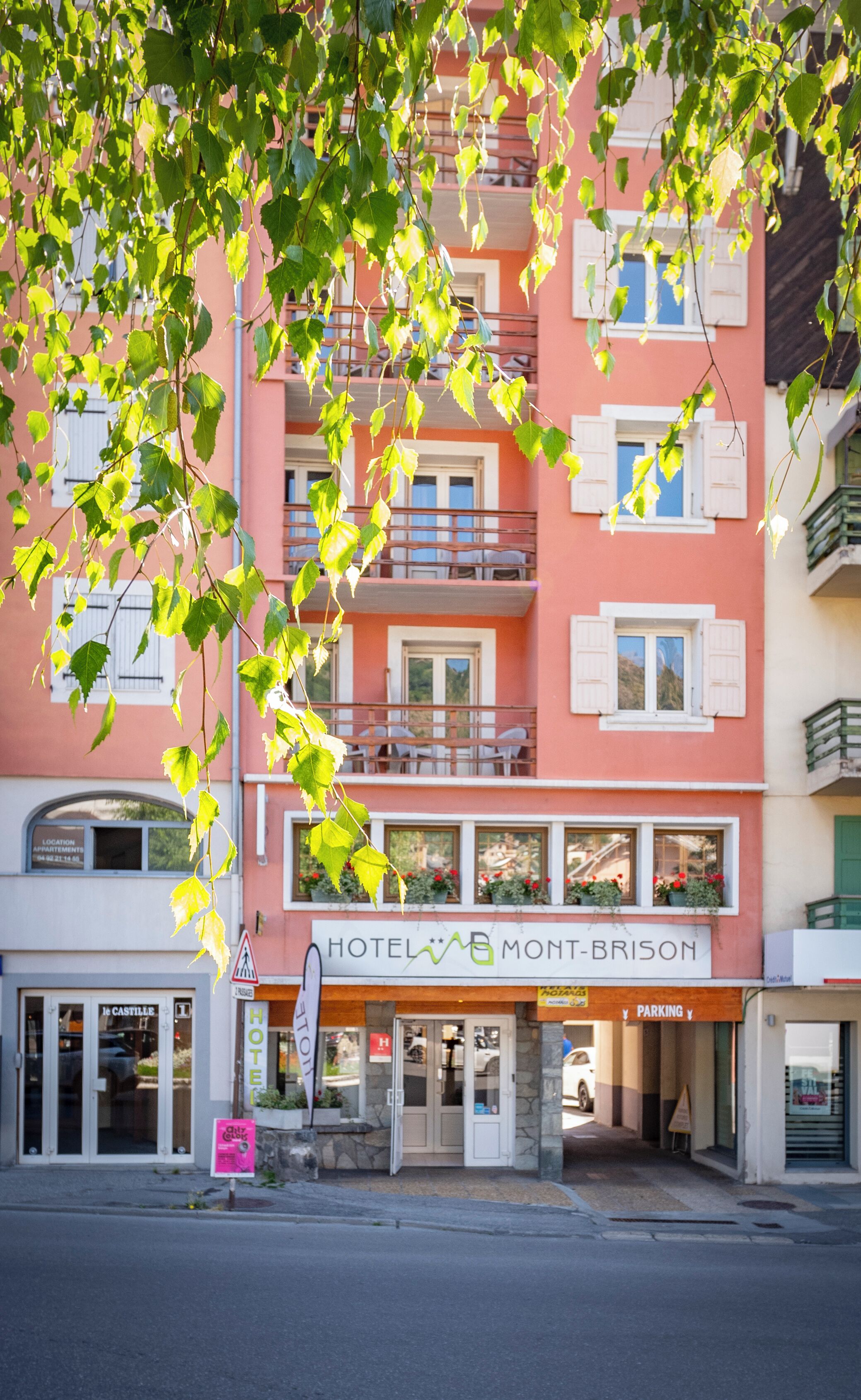 Un hotel con facciata rosa, balconi con ringhiere bianche e un cartello che riporta la scritta "HOTEL MONT-BRISON".