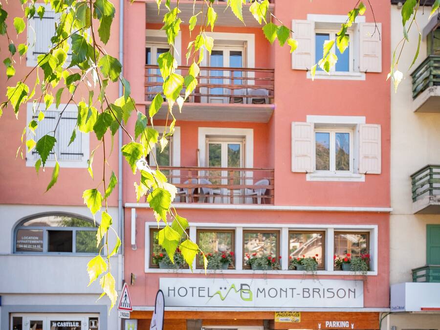 Un hotel amb façana rosa, balcons amb baranes blanques i un rètol que diu "HOTEL MONT-BRISON".