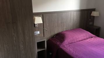 Una habitación de hotel con cama, mesita de noche, lámpara y armario.