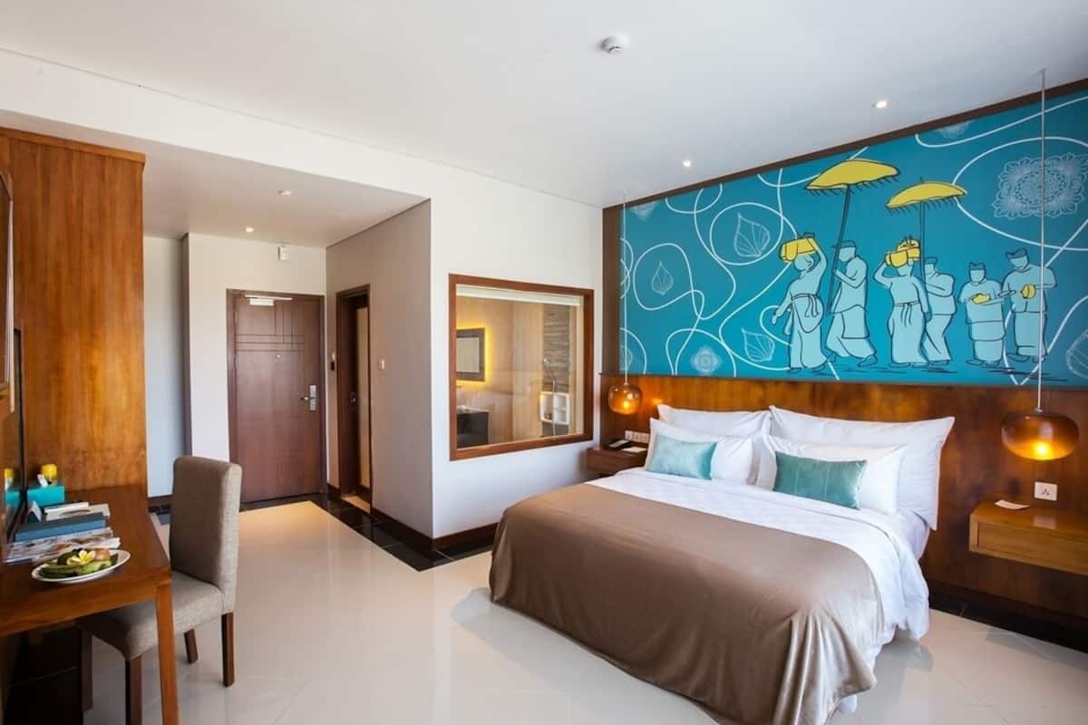 A modern hotel room with a large bed, a desk with a chair, and a wall with a blue abstract design.