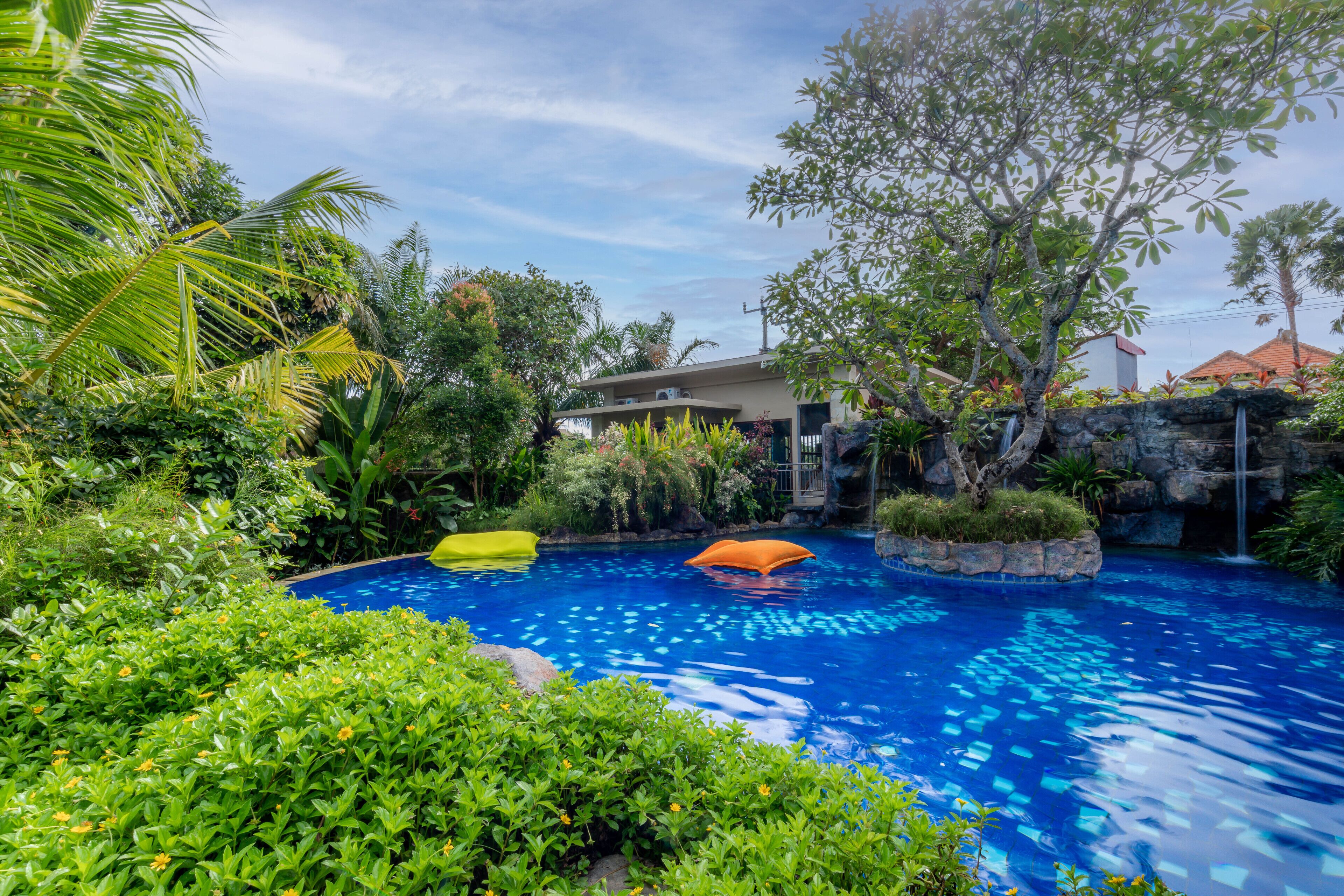 A swimming pool surrounded by lush greenery and a building in the background.