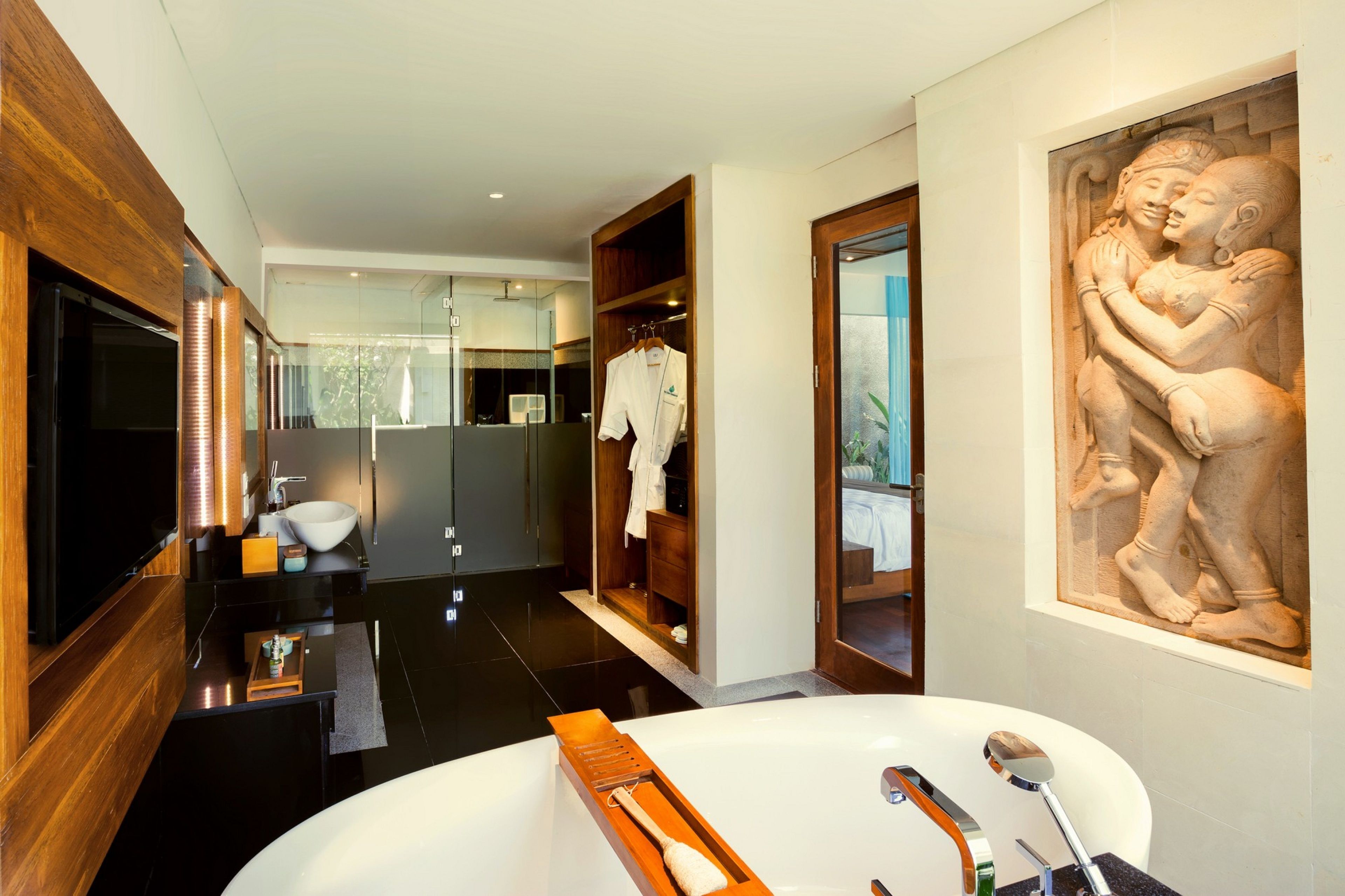 A modern bathroom with a large bathtub, wooden vanity, and a stone sculpture.
