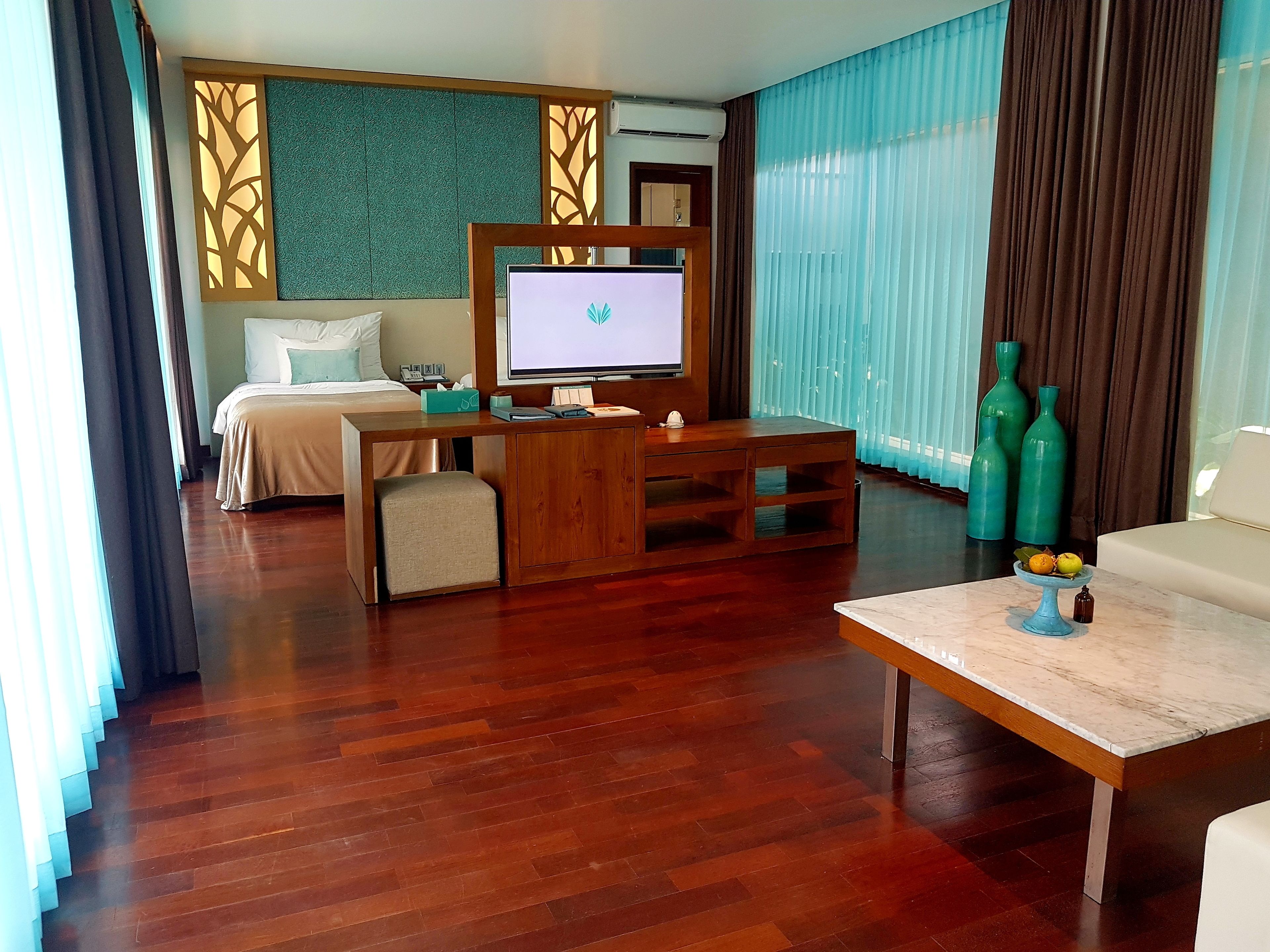 Habitación de hotel con cama, escritorio con computadora, televisor y zona de estar con mesa.