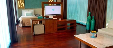 Habitación de hotel con cama, escritorio con computadora, televisor y zona de estar con mesa.