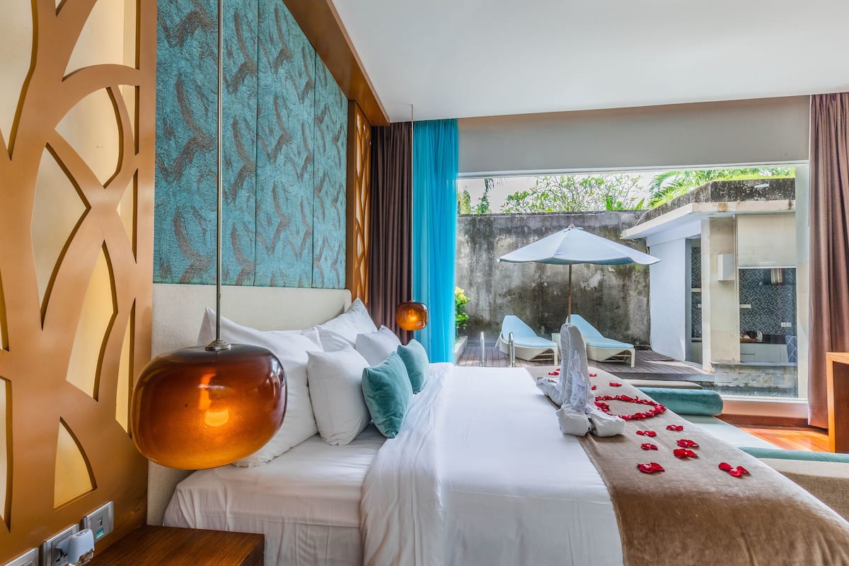 A hotel room with a large bed, a view of the outdoor area, and a balcony with a table and chairs.