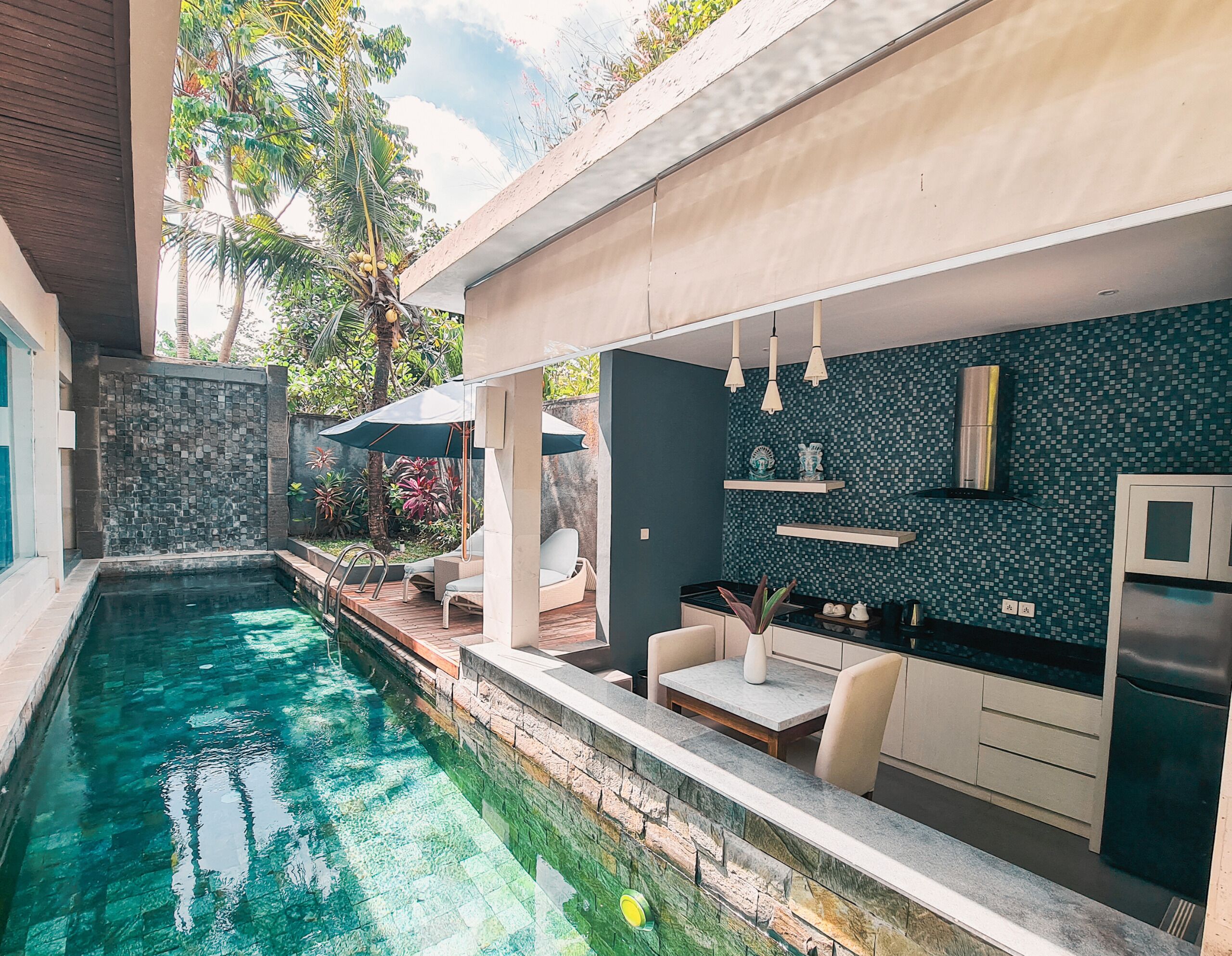 Une cuisine extérieure moderne avec une piscine, entourée de verdure et d’un mur en pierre.