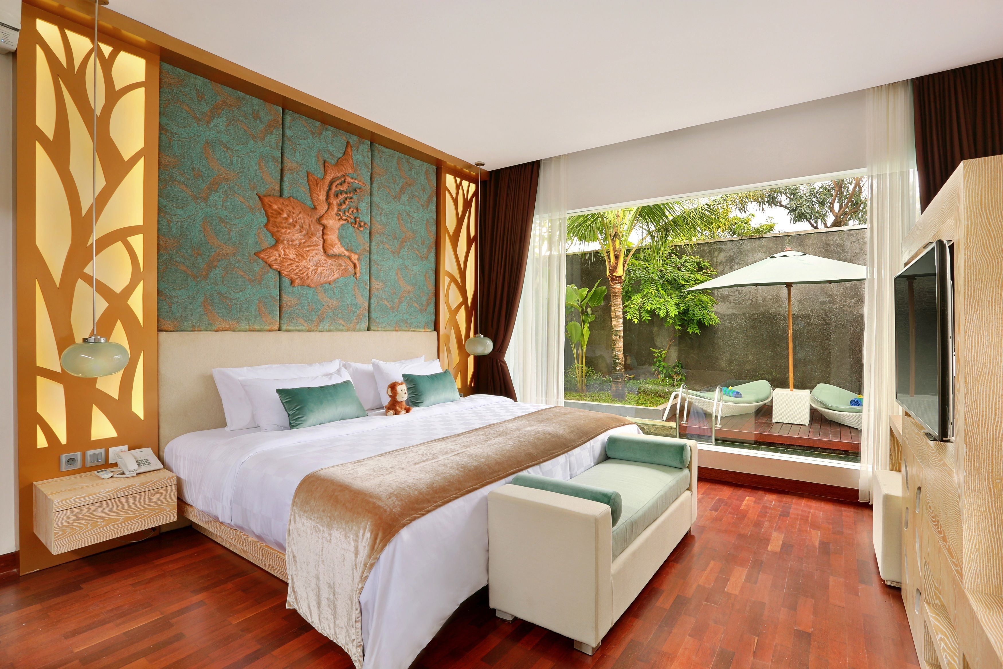 A modern bedroom with a large bed, a sofa, a TV, and a view of a garden through a glass door.