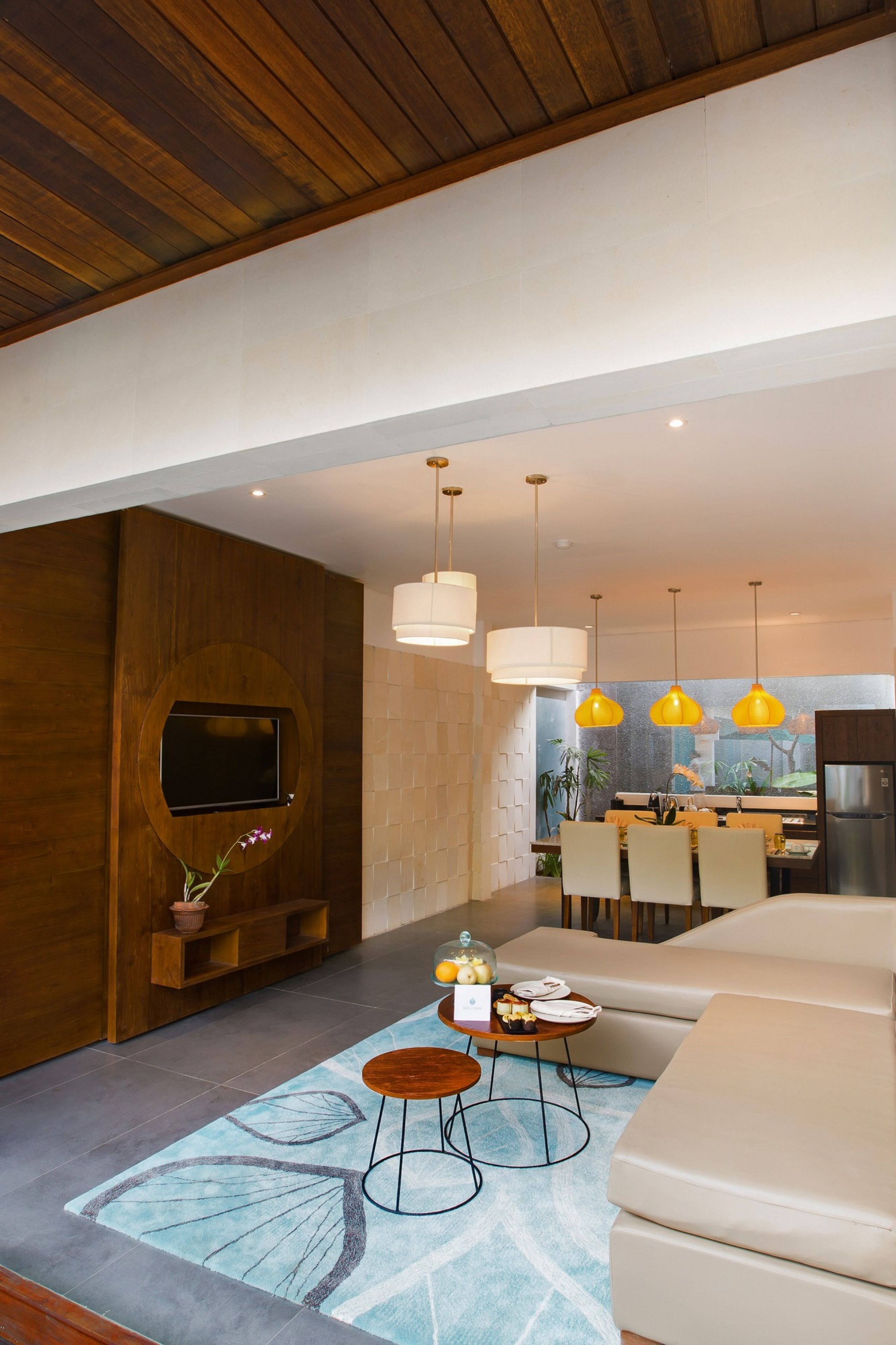 Een moderne woonkamer met een flatscreen televisie, houten lambrisering, een eethoek en een keuken op de achtergrond, en een grote bank.