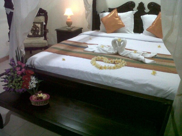 Una cama bien tendida con un arreglo floral, una mesita de noche con una lámpara y un pequeño objeto decorativo.