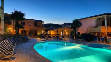 Una piscina con lettini, un solarium piastrellato e edifici con facciate dai toni caldi.