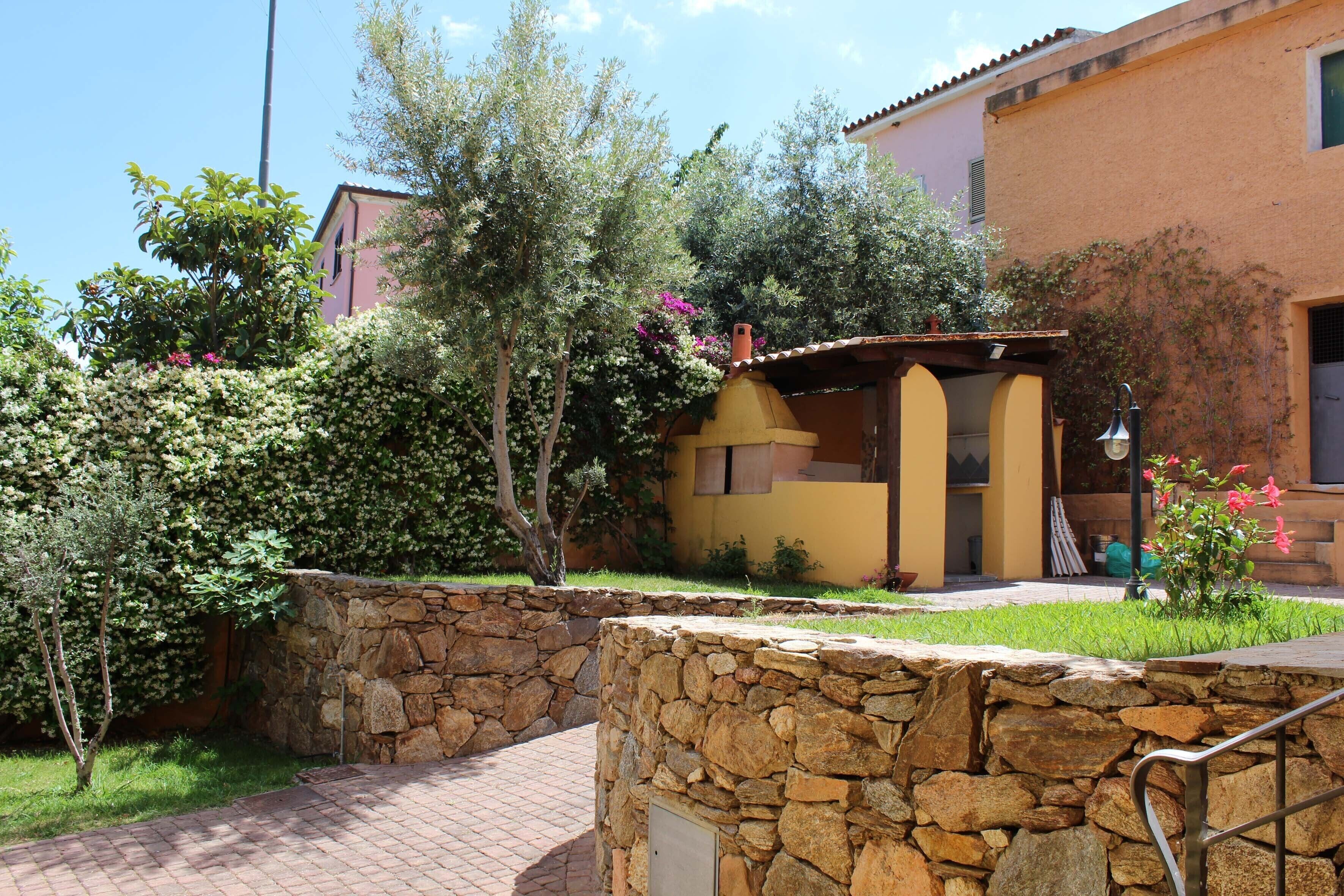 A stone wall with a metal handrail, a paved walkway, and a yellow building with a small porch.