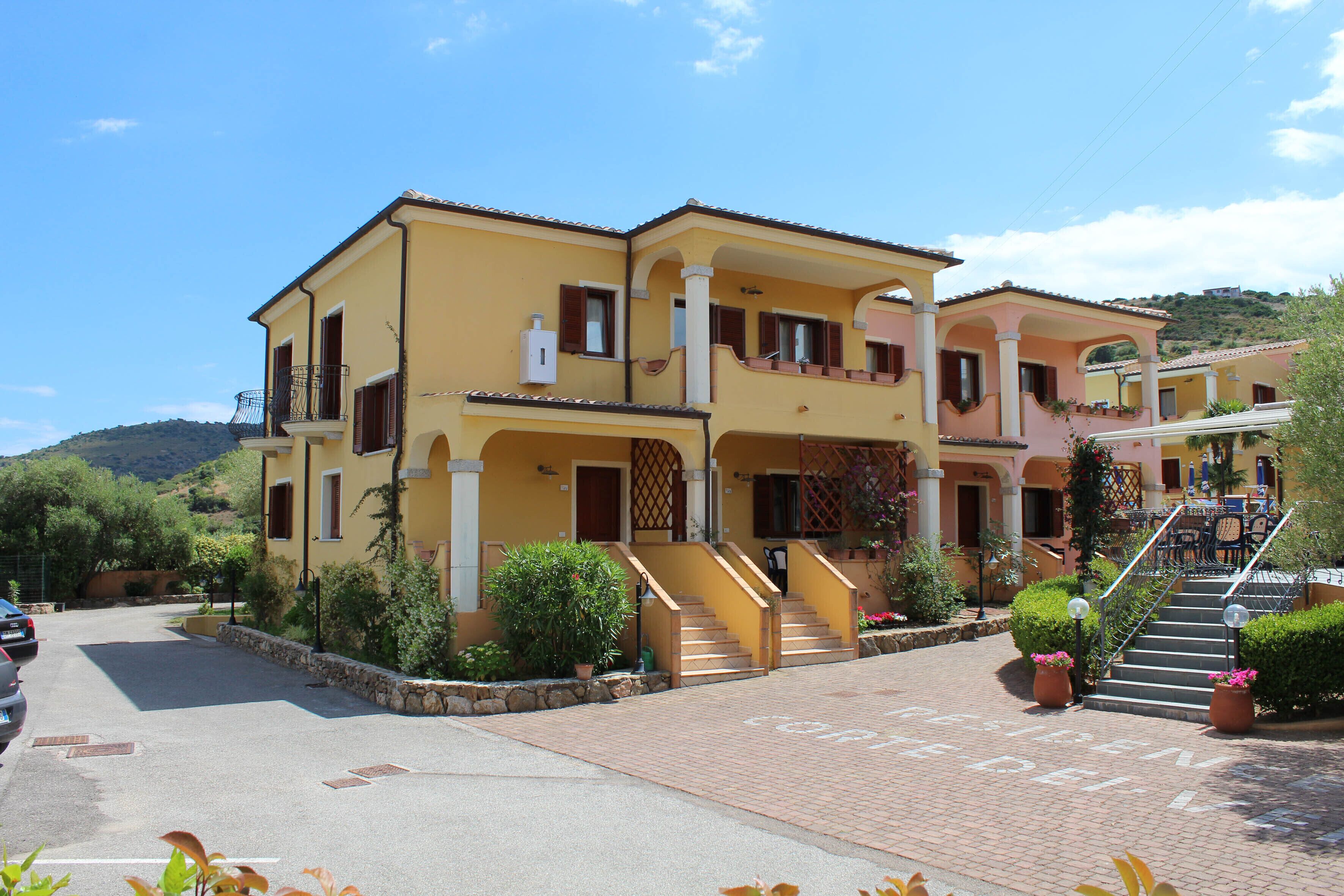 A two-story yellow building with a central staircase and a covered outdoor seating area.
