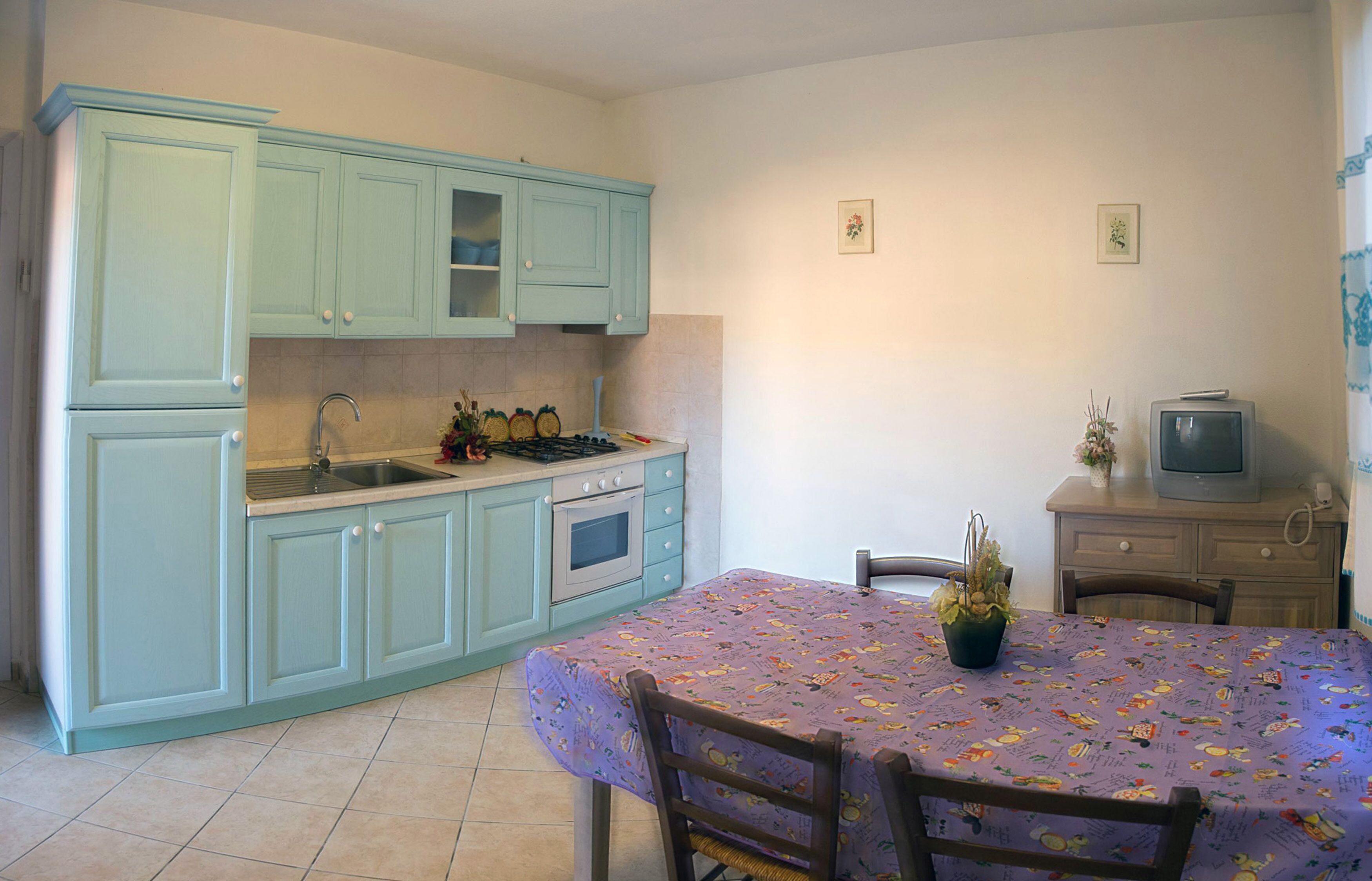 A kitchen with light blue cabinets, a sink, stove, and a dining table with a floral tablecloth.
