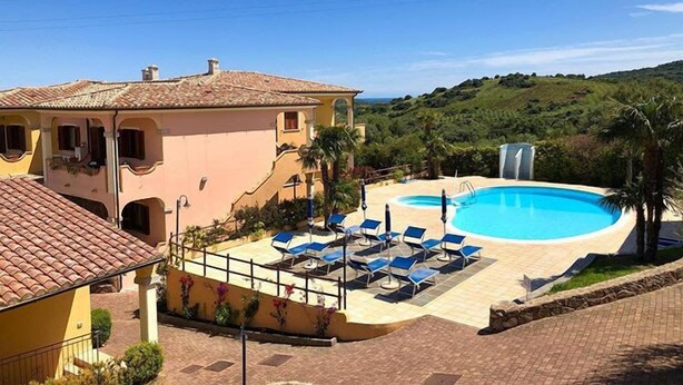 A villa with a swimming pool, sun loungers, and a view of the hills. - Residence Corte dei Venti (Budoni)