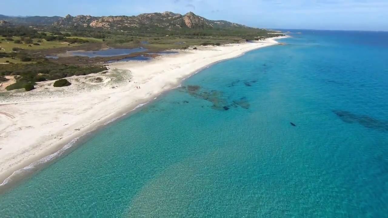 A coastal landscape with a sandy beach and clear blue waters.