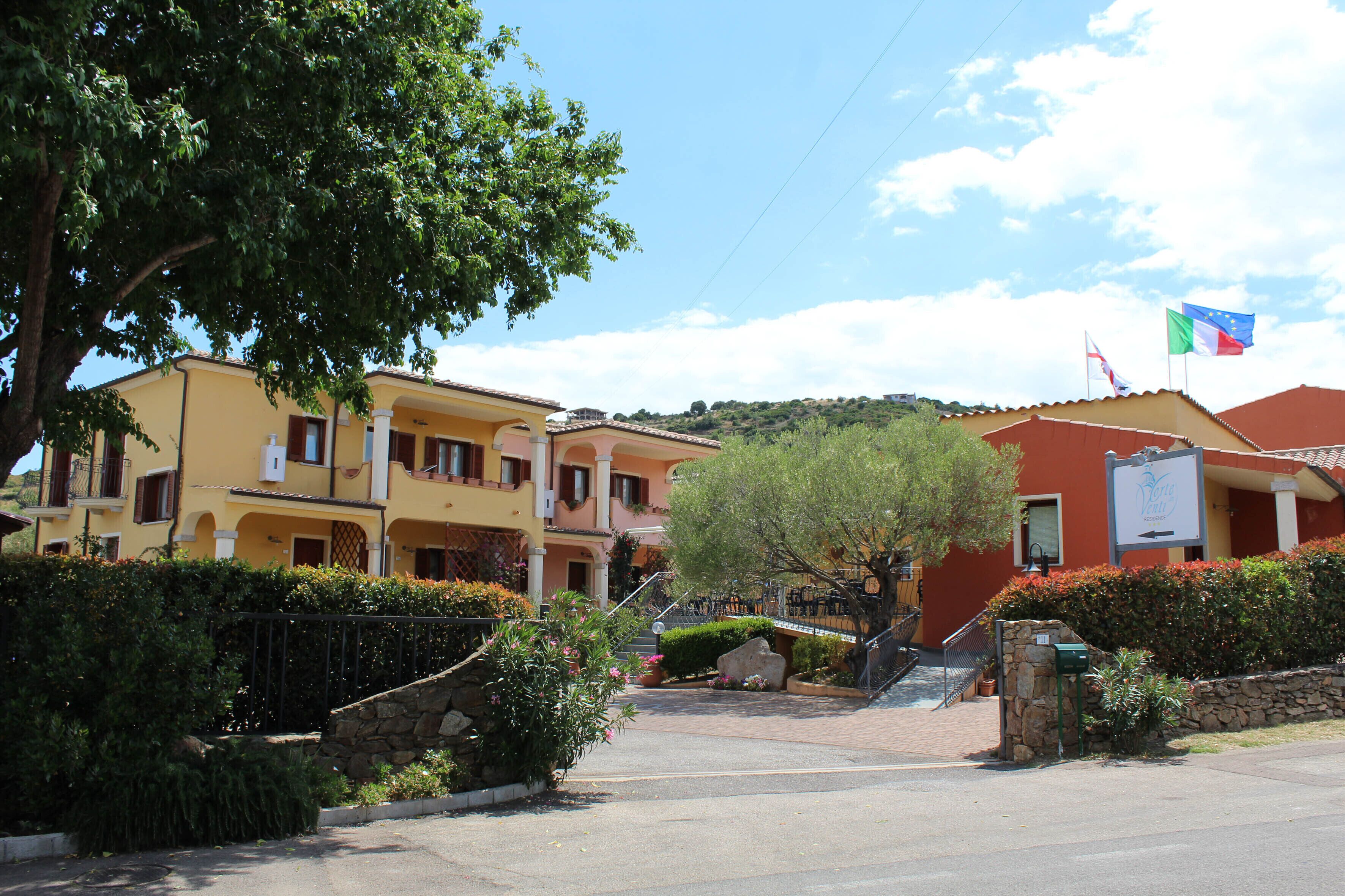 A row of yellow and red buildings with a stone wall and a tree in the foreground.