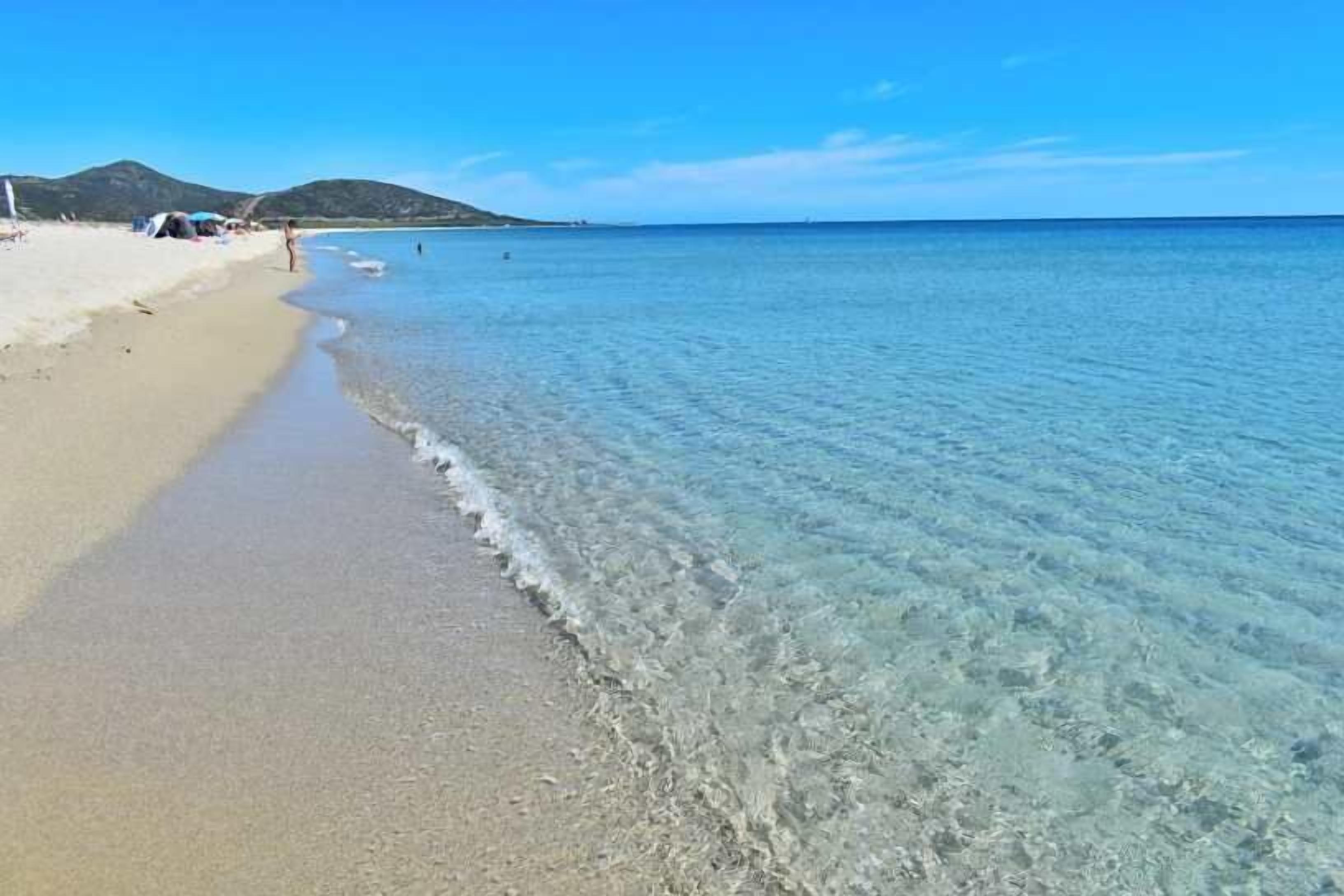 Una spiaggia con acque cristalline, una costa sabbiosa e una montagna sullo sfondo.